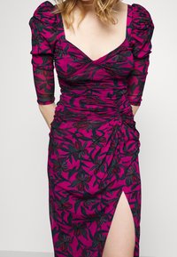 Fuchsia klänning med trekvarts puffärmar, rynkad design och svart blommönster; har en hög slits på vänster sida.