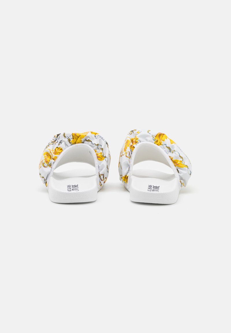 Witte instapsandalen met een bloemenpatroon in het geel, voorzien van geplooid materiaal rondom de bovenkant en een platte, gestructureerde zool.