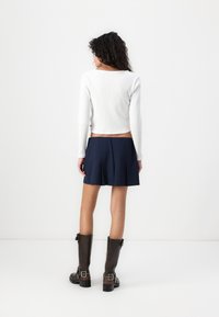 White ribbed long-sleeve top paired with a navy pleated skirt and brown knee-high boots with buckle accents. Minimalistic design.