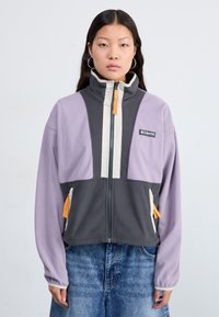 Fleece jacket in lavender and gray, zippered front, high collar, side pockets with orange accents, and logo patch on chest.