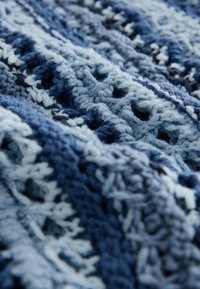 Blaues Häkelgewebe mit unterschiedlichen Blautönen, komplizierten Mustern und einer strukturierten Optik mit offenen Webabschnitten.