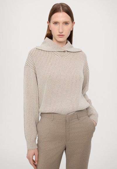 Beige ribbed sweater with wide collar and button details. Paired with light brown tailored trousers, smooth texture and fitted silhouette.