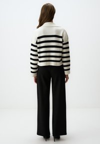 Maglione a maglia con righe orizzontali bianche e nere, dotato di colletto e design corto. Abbinato a pantaloni neri a gamba larga.