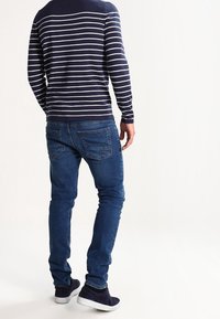 Camisa de rayas azul marino y blanca de manga larga combinada con jeans azules y zapatillas oscuras, vista desde la parte posterior. Textura suave, ajuste casual.