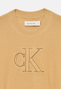 Πουλόβερ Calvin Klein Jeans σε ανοιχτό καφέ με ριγωτό στρογγυλό λαιμό. Διαθέτει το κεντημένο λογότυπο "CK" σε πιο σκούρο νήμα. Υφασμάτινη υφή.
