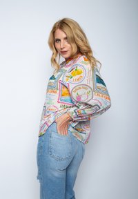 Leichte, bedruckte Bluse mit fruchtigen Designs in lebhaften Farben; hat lange Ärmel, eine lockere Passform und elastische Bündchen. Getragen mit Jeans.