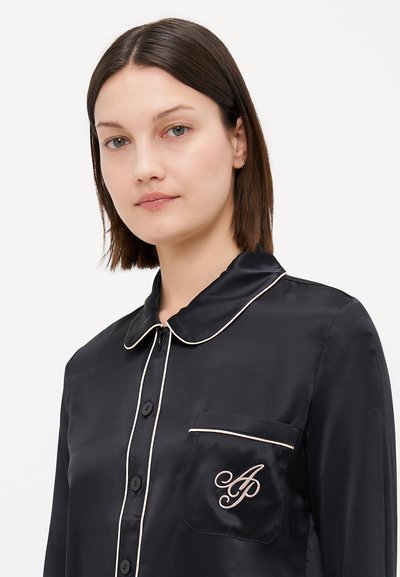 Black satin pajama shirt with a collar, button front, and pocket. Features white piping and embroidered initials on the pocket.