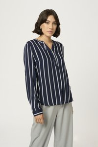 Blusa a rayas azul marino con escote en V, mangas largas, detalle de botones y tela ligera, combinada con pantalones gris claro.