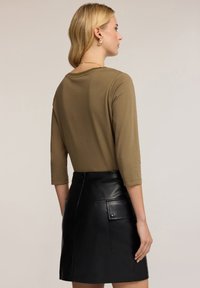 Olivově zelený top s třičtvrtinovými rukávy, který je kombinován s černou skládanou sukní z umělé kůže, jež má boční kapsu a obepínající siluetu.