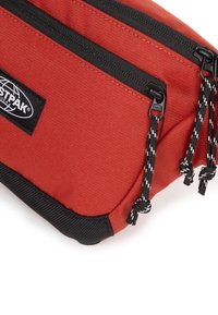 Rode stoffen zak met twee aparte ritscompartimenten, zwarte accenten en zwart-witte trekkoorden. Heeft een logopatch.