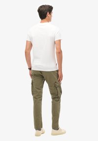 Camiseta blanca de algodón combinada con pantalones cargo verde oliva que presentan múltiples bolsillos, piernas rectas y un ajuste relajado, contrastados con zapatillas ligeras.