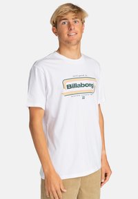 White cotton t-shirt featuring a central graphic in green and orange with "Billabong" text. Short sleeves and a round neckline.