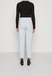 Svart långärmad topp, ljusblå högmidjade byxor och marinblå klackskor sedd bakifrån. Byxorna har bakfickor och en subtil lyster.