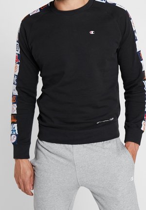 Sudadera negra con parches de logotipo coloridos del equipo a lo largo de las mangas; presenta un cuello redondo, puños acanalados y una etiqueta de logotipo en el dobladillo.
