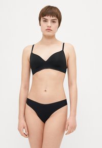 Black bra and bikini set made of smooth fabric. Bra features a scalloped lace band and adjustable straps, with a plunging neckline design.