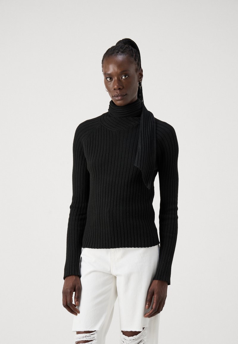 Must mustriba turtleneck-sweater koos kinnitatud salliga, millel on keha lähedane siluett ja pikad varrukad. Kombineeritud kulunud valgete teksadega.