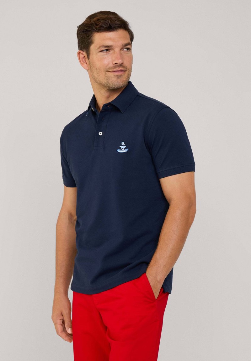 Granatowa koszulka polo z bawełny, z klasycznym kołnierzykiem i zapięciem na dwa guziki, z jasnoniebieskim haftowanym logo na piersi.