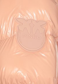 Giacca in pesca lucida e imbottita con toppa del logo in rilievo che presenta due uccelli e la scritta "PINKO", che evidenzia una texture liscia e brillante.