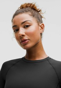 Must värvi sportlik ülemine, millel on hästi istuv disain, pikad varrukad ja ümmargune kaelus. Sile kangas koos peente õmblusdetailidega, mida kannab mudel.