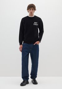 Felpa nera con la scritta "NOT TODAY" in bianco sul petto, abbinata a jeans blu e scarpe nere, su uno sfondo semplice.