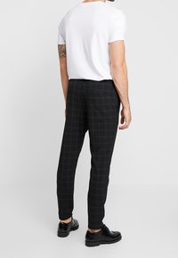 Svarta rutiga byxor med smal passform, sidofickor och en bakficka. Bärs med en enkel vit t-shirt och svarta skor.