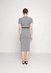 Abito midi grigio a coste con maniche corte e silhouette aderente. Presenta una cintura brandizzata nera e sandali con tacco alto eleganti.
