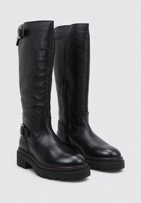 Botas de cuero negras hasta la rodilla con acabado texturizado, punta redonda, suela gruesa, cierre lateral y acento decorativo de hebilla.