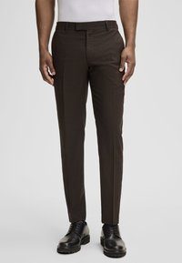 Braune, maßgeschneiderte Hose mit glatter Textur, klassischem Schnitt, flacher Vorderseite und Gürtelschlaufen. Kombiniert mit schwarzen Schnürschuhen.