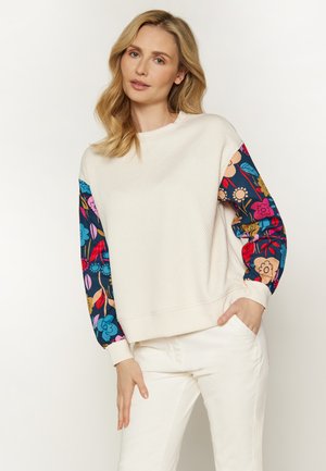 Helles Creme Sweatshirt mit Fischgrätstruktur, mit bunten, floral gemusterten Ärmeln in Pink-, Blau- und Grüntönen.