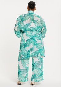 Transparentes, gemustertes Outfit im grünen Blumendesign, bestehend aus einer langen Jacke und weiten Hosen, aus leichtem, fließendem Stoff.