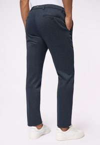 Marineblaue maßgeschneiderte Hose mit feiner Textur, slim fit, seitlichen Taschen und einer Gesässtasche, kombiniert mit weißen Sneakers.