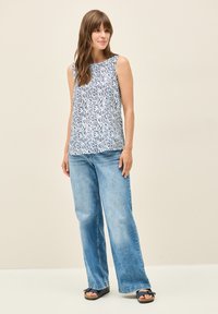 Ärmelloses Oberteil mit weißem Grund und navyblauem, abstraktem Blattmuster, kombiniert mit hellblauen, weit geschnittenen Jeans und dunklen Sandalen.