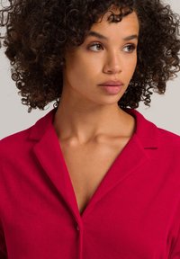 Camisa roja de botones con cuello, con una textura suave y mangas cortas, exhibida en una persona con cabello rizado.