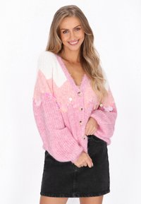 Przesadny różowy sweter z dzianiny z białym wzorem w zygzak, dużymi guzikami oraz cekinowymi zdobieniami. Zestawiony z czarną spódnicą dżinsową.