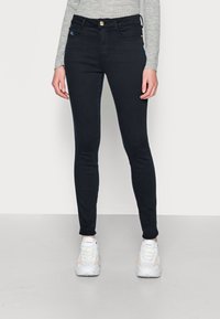 Jeans de corte ajustado, de color azul oscuro con textura acanalada, de cintura alta, diseño de cinco bolsillos y cierre de botón dorado en la parte delantera.