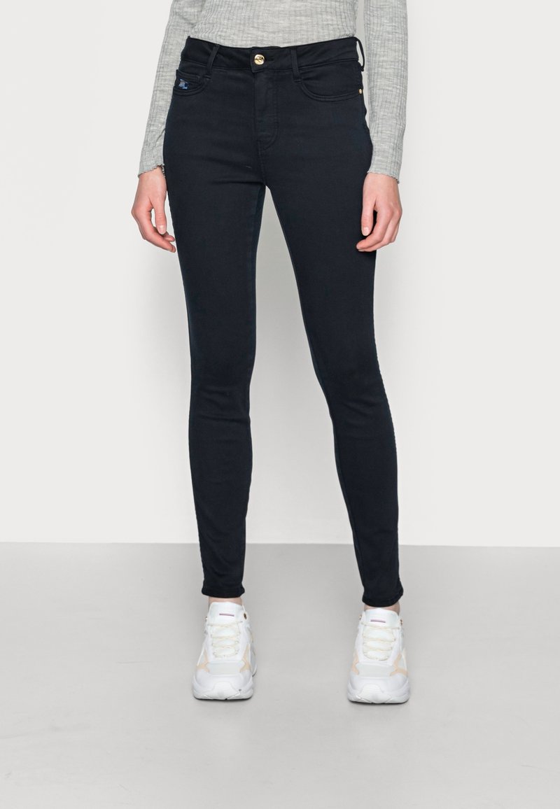 Jeans de corte ajustado, de color azul oscuro con textura acanalada, de cintura alta, diseño de cinco bolsillos y cierre de botón dorado en la parte delantera.