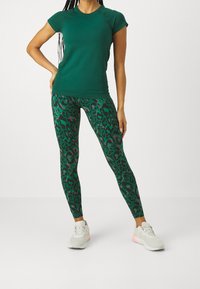 Grön tight t-shirt med korta ärmar, kombinerad med gröna leggings i leopardmönster. Leggings har rosa detaljer och är tillverkade av ett elastiskt material.