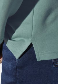 Mint green short-sleeved top with ribbed texture, featuring a side slit hem, paired with dark blue denim fabric showing subtle detailing.