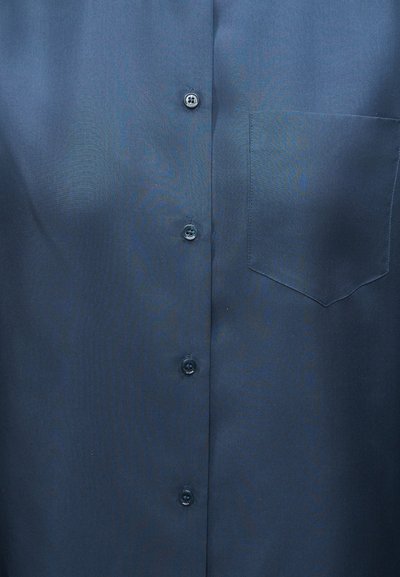 Πουκάμισο σε χρώμα σκούρο μπλε με τέσσερα εμφανή κουμπιά και μία τσέπη στο στήθος στο δεξί μέρος.