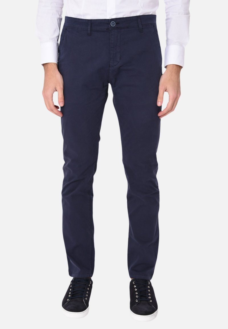 Chinos in cotone blu navy con vestibilità slim, dotati di chiusura con zip, tasche laterali e chiusura con bottone. Indossati con sneakers nere.