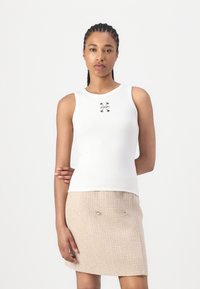 Weißes, geripptes Tanktop mit kleinem schwarzem "JOOP!"-Logo auf der Vorderseite. Kombiniert mit einem strukturierten, beigen Rock mit silbernen Akzenten.