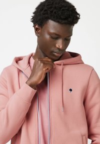 Roze hoodie met een voorrits, capuchon met trekkoord en navy boomlogo accent. Katoenen mix stof met een zachte textuur en geribde boorden.