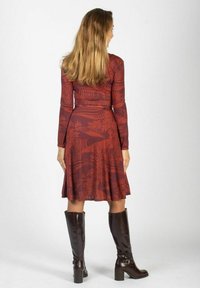 Sukienka z długim rękawem w ciemnoczerwonym kolorze z kwiatowym wzorem. Rozkloszowana spódnica, dopasowana talia, zestawiona z błyszczącymi brązowymi kozakami do kolan. Prosty fason.