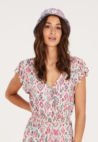 Bloemmotieven jurk met korte rimpel mouwen, een diepe V-hals en een elastische tailleband. Voorzien van een bijpassende bucket hat met vergelijkbare patronen.