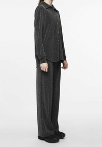 Set di loungewear nero e luccicante composto da una camicia con bottoni e colletto e pantaloni larghi. Le scarpe con suola testurizzata completano il look.