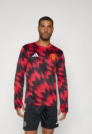 Langemouws rood en zwart voetbalshirt met zigzagpatroon, voorzien van Adidas-strepen, Manchester United-logo en zwarte shorts.