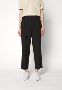 Černé široké kalhoty s předními sklady, vyrobené z hladkého materiálu. V kombinaci s béžovým topem s krátkým rukávem a bílými teniskami.