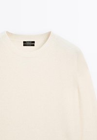 Cream-colored cashmere sweater with a ribbed crew neckline and soft texture. Labels indicate brand and material composition.