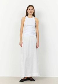 Wit geribbeld tanktop gecombineerd met een luchtige witte maxi rok met zijsplitten, aangevuld met zwarte geclipte slip-on schoenen.