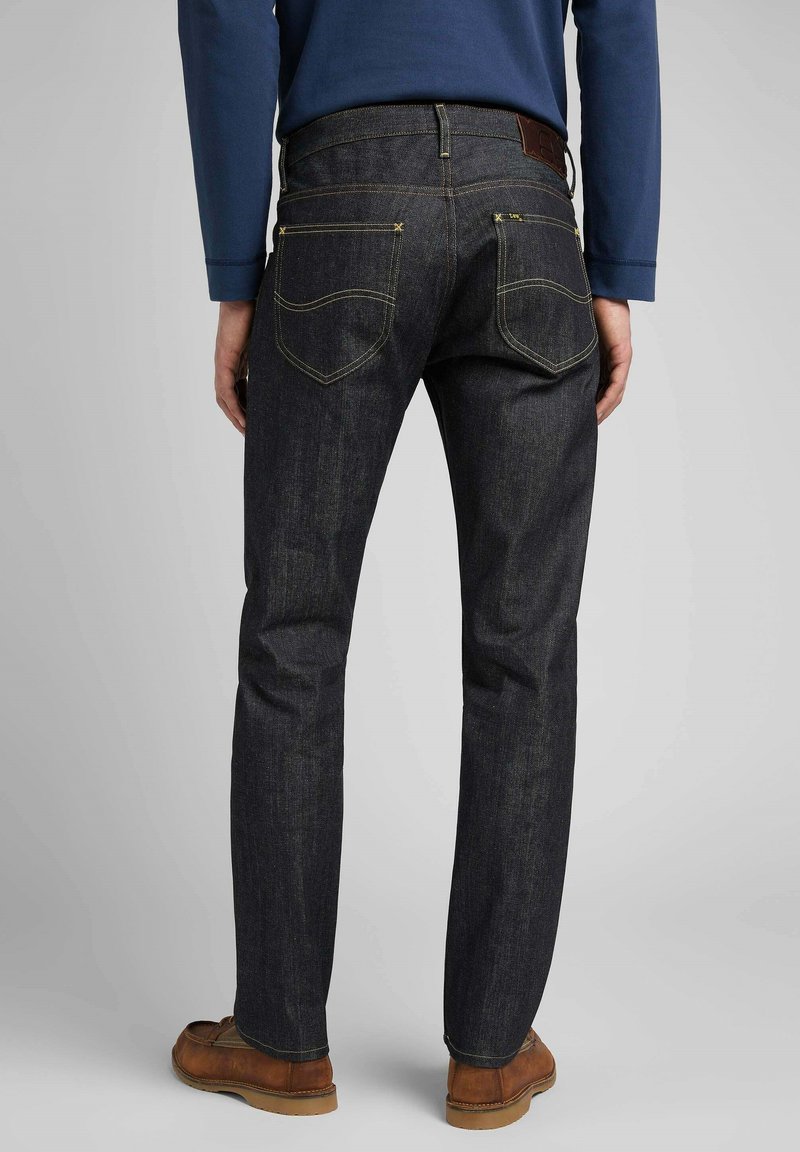 Los jeans de mezclilla azul oscuro presentan un diseño de pierna recta, detalles de costura amarilla, una etiqueta de cuero marrón en la parte trasera y dos bolsillos traseros de parche.